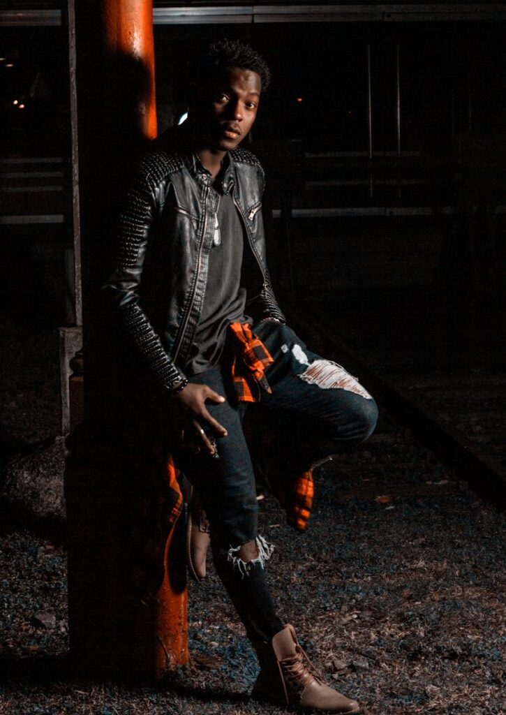 A fashionable man strikes a pose at night in a trendy leather jacket and ripped jeans.