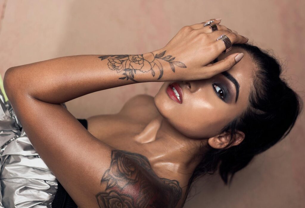 Close-up portrait of a tattooed woman with eye makeup and red lips posing in an editorial shoot.