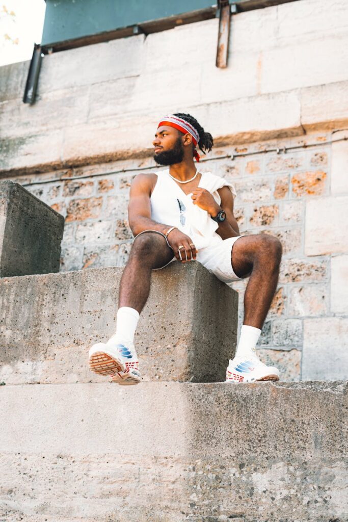 Stylish man with beard poses confidently in trendy streetwear, sitting on urban concrete steps.