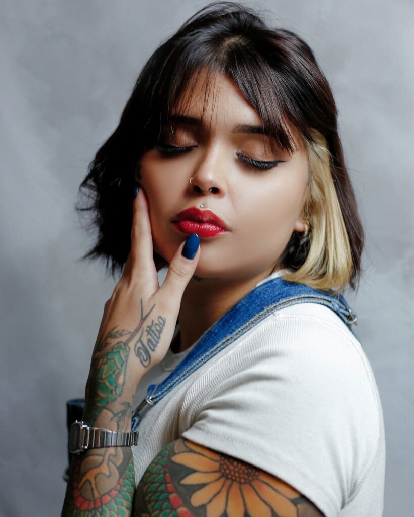 Portrait of a tattooed woman with vibrant makeup posing in a studio setting, showcasing style and expression.