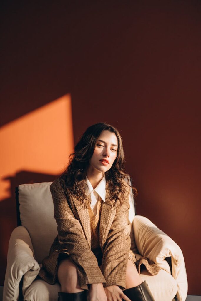 Woman in stylish outfit relaxing in a cozy studio setting with warm lighting.