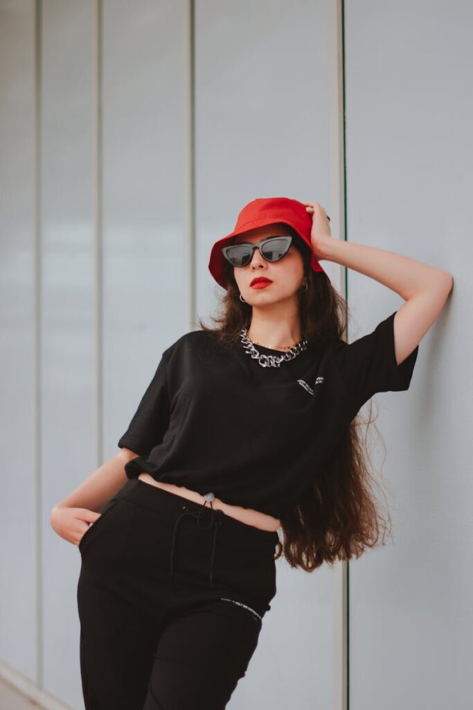 Elegant fashion portrait of a woman in a red hat and sunglasses against a minimalist backdrop.
