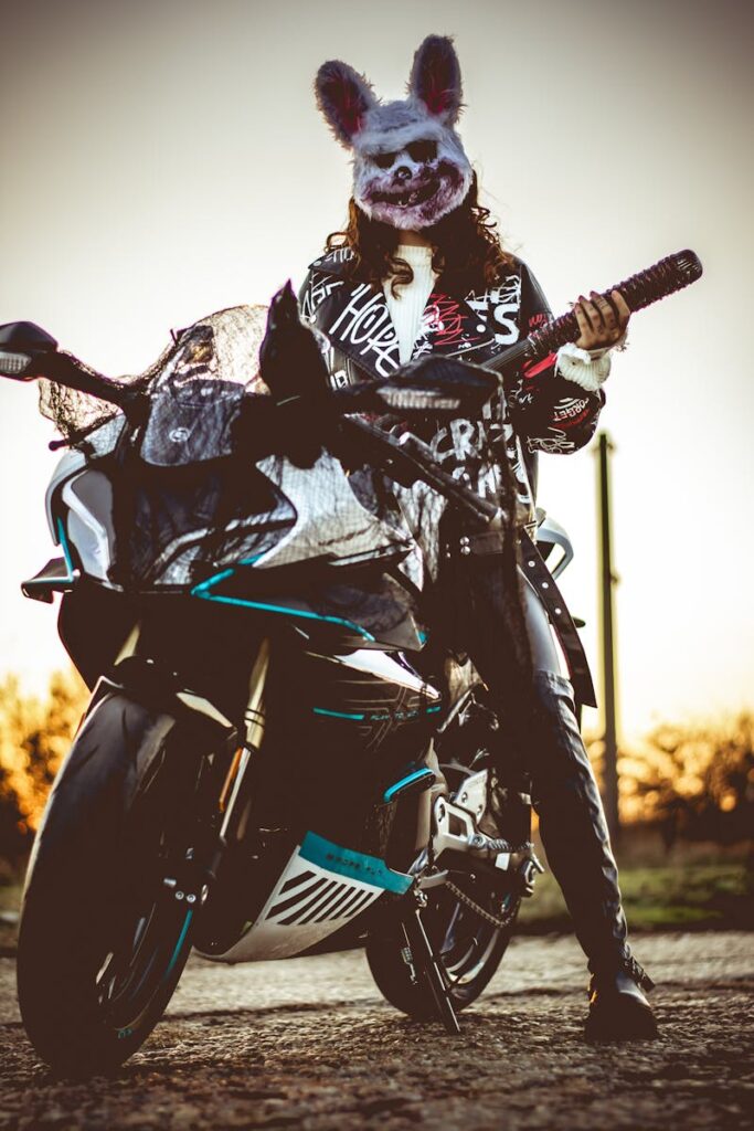 Masked biker with sword standing by motorcycle, sunset scene.