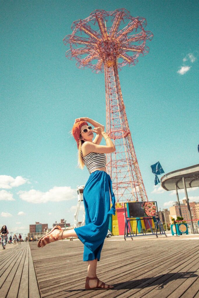 Young woman in vibrant outfit posing near iconic Coney Island tower.