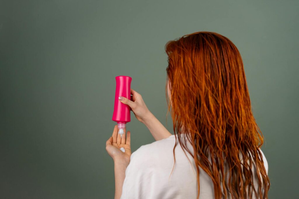 Adult woman with wet red hair applying conditioner. Hair care routine.