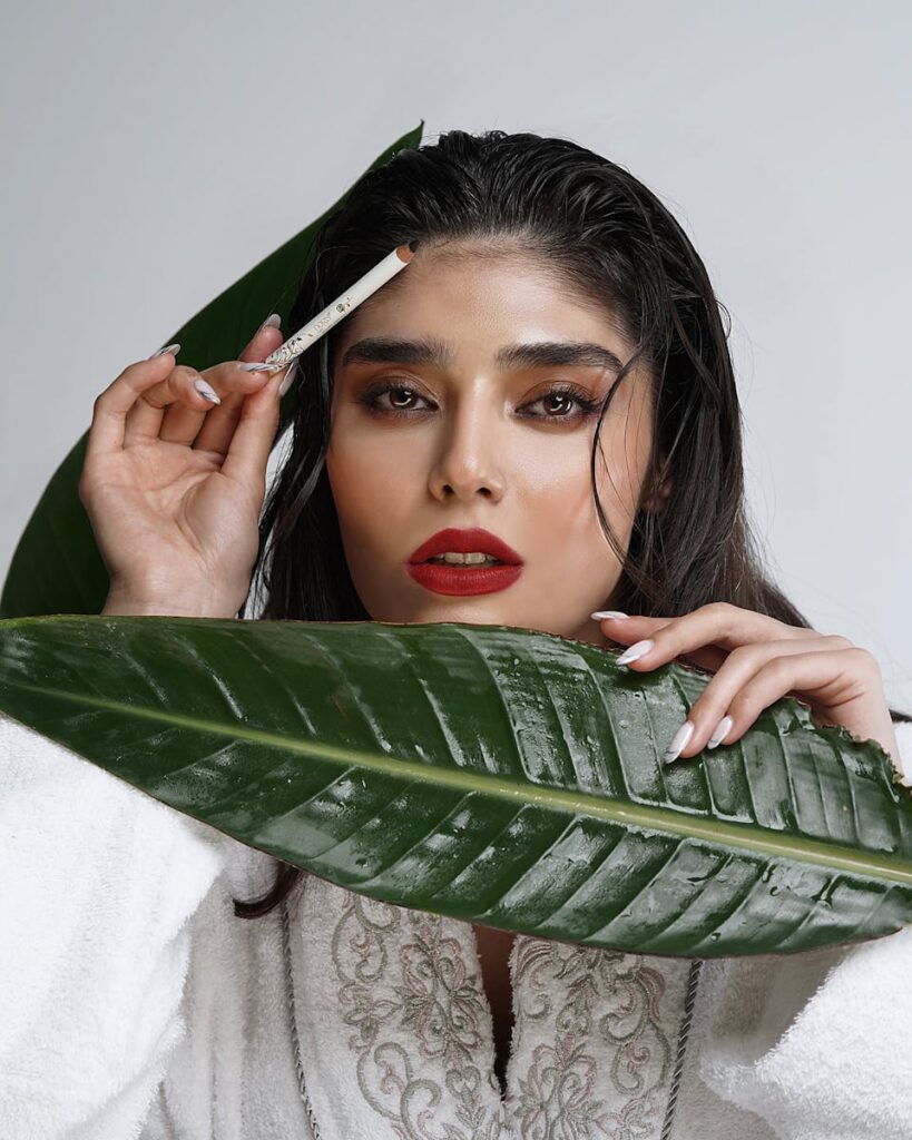 Fashion portrait of a woman featuring a tropical leaf and makeup brush for natural beauty theme.