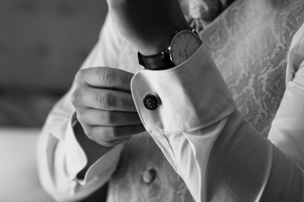Stylish black and white photo of a man adjusting his cufflinks, highlighting elegance and sophistication.