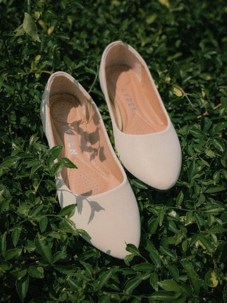 Stylish white flat shoes placed on lush green foliage, ideal for weddings and events.