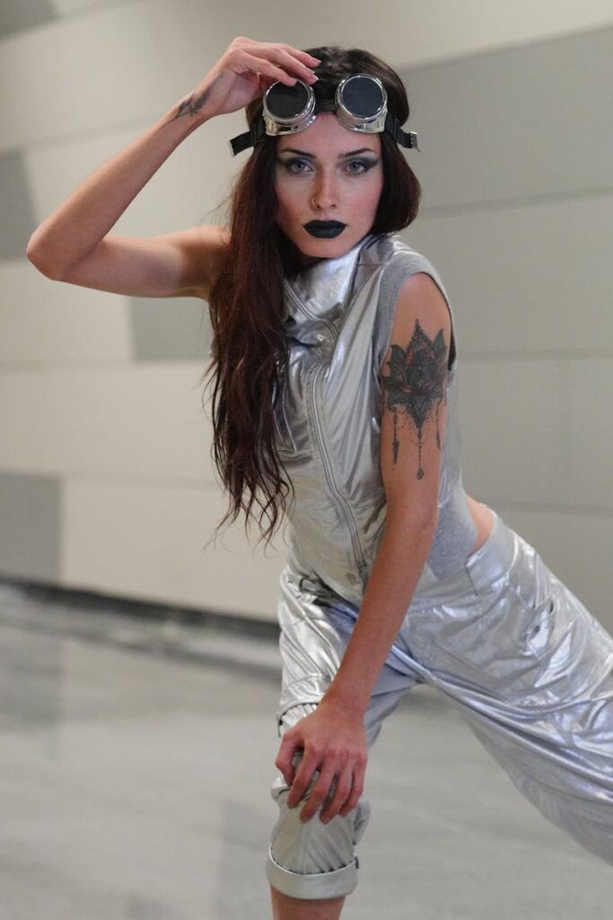Stylish model in silver attire with goggles, showcasing edgy fashion and dark makeup.