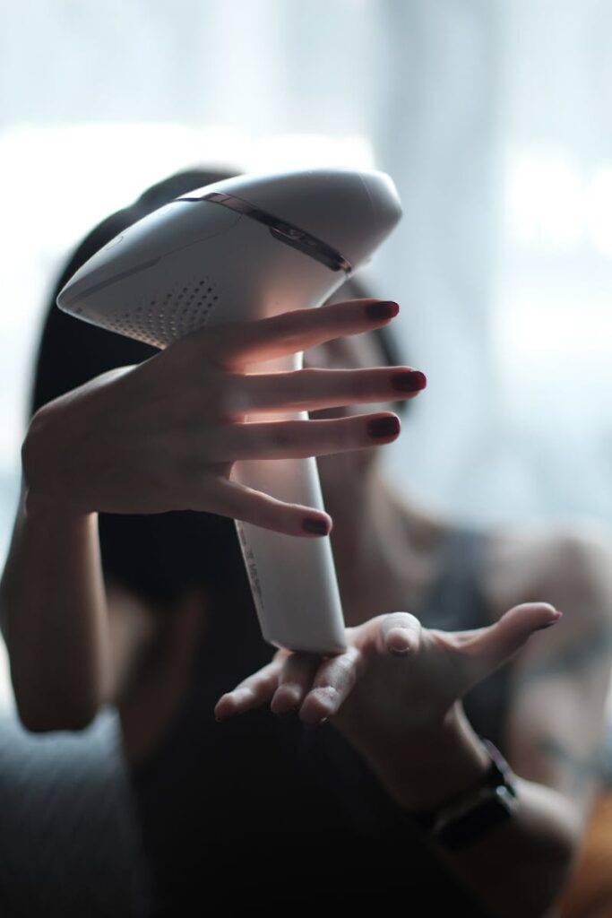 A woman surrounded by soft light holds an IPL hair removal device with elegance.