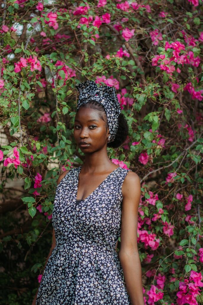 Young woman in a floral dress standing beside vibrant pink bougainvillea. A serene outdoor portrait.