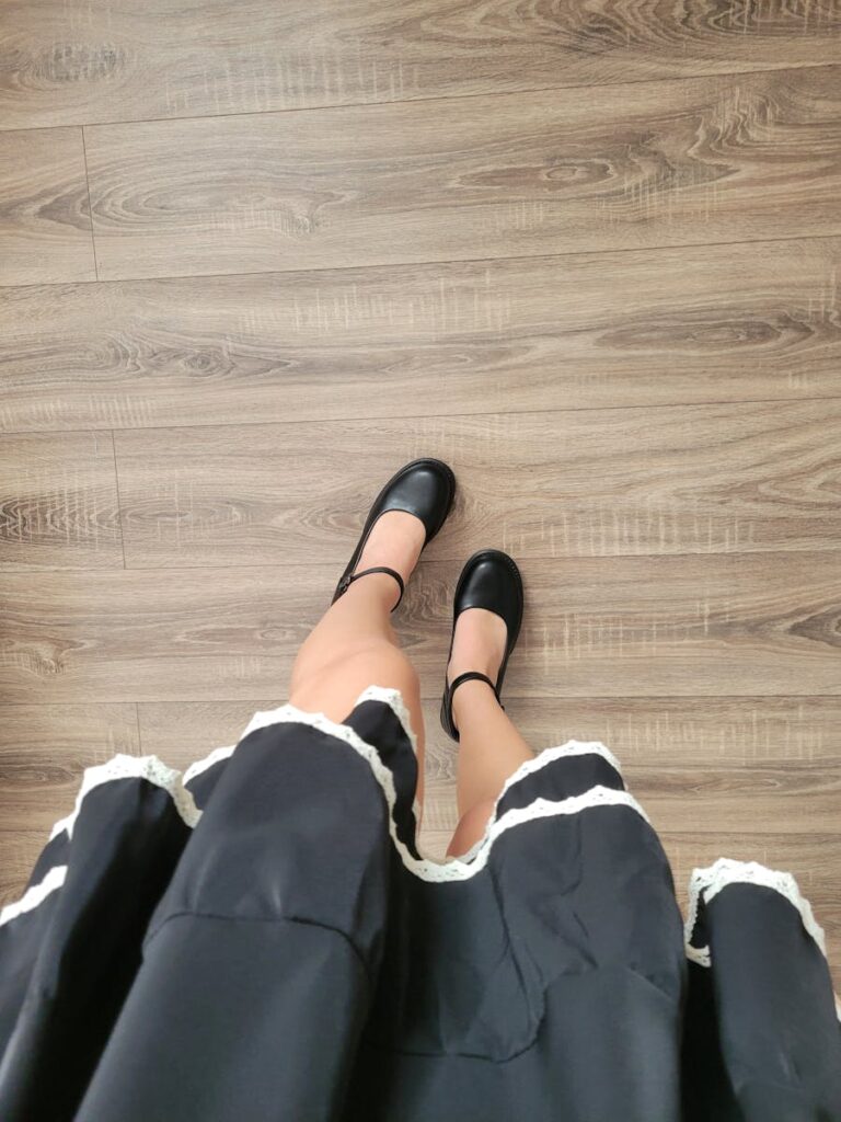 View of black shoes and dress on a wooden floor, minimalist style.