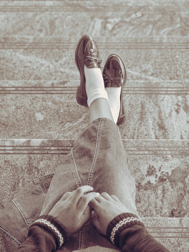Vintage-styled top view of person sitting on steps with loafers and denim skirt.