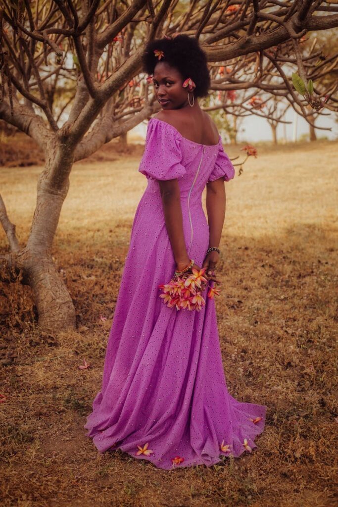 African woman in a flowing purple gown standing gracefully under autumn trees.