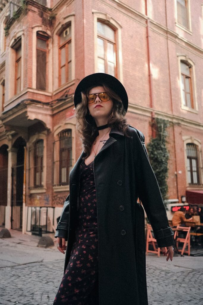 Fashionable woman in black coat and hat poses on an urban street with vintage architecture.