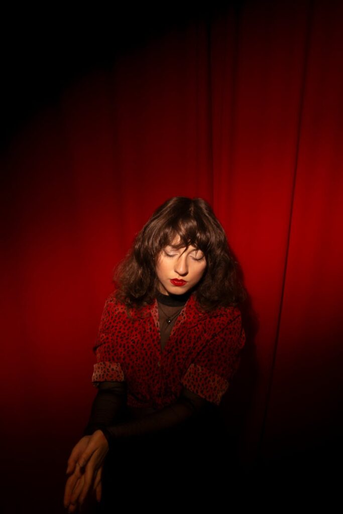 A striking portrait of a woman in red with dramatic lighting against a vibrant red curtain backdrop.