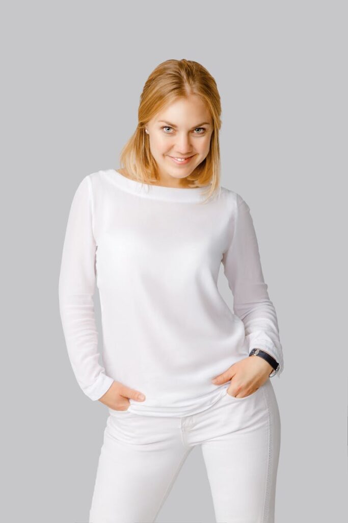 Portrait of a smiling Caucasian woman in a white outfit against a grey background, exuding confidence.