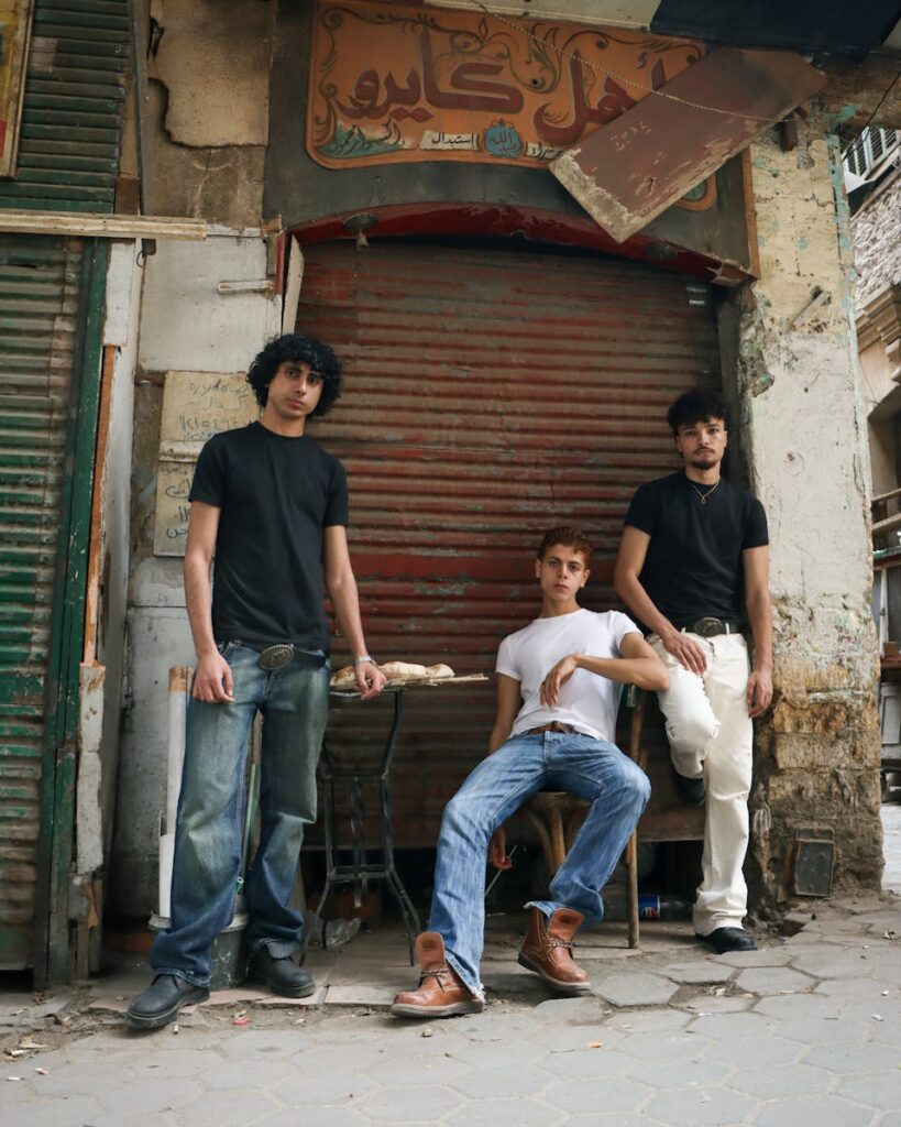 Three young men pose in front of a closed shop in Cairo, showcasing casual fashion.