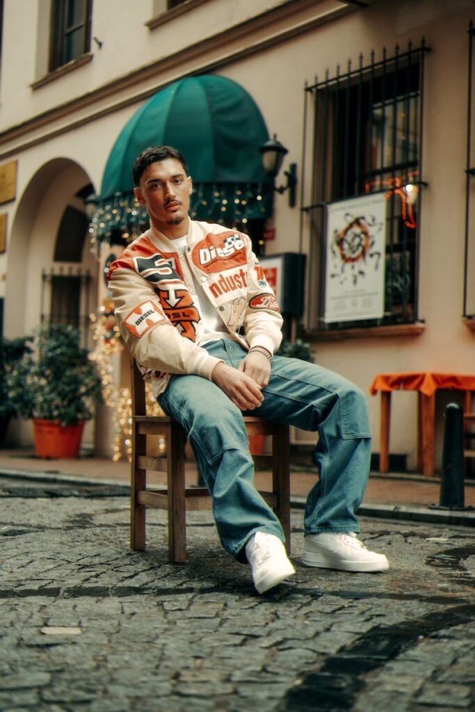 Casual young adult sitting on a chair in a vibrant urban setting with cobblestone street.