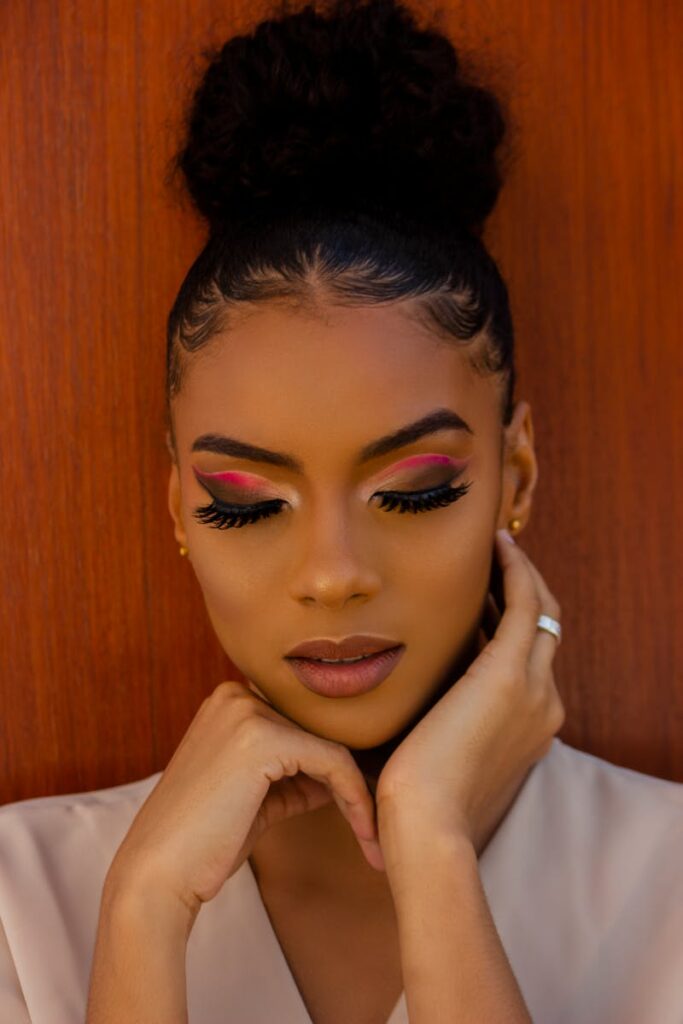 Close-up portrait of a woman with elegant hairstyle and vibrant eye makeup against a wooden background.