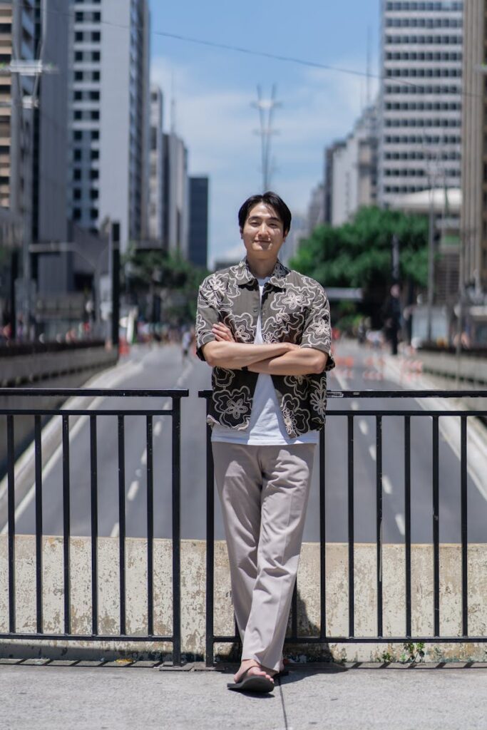 A man in casual attire stands confidently on a bridge with skyscrapers in the background.