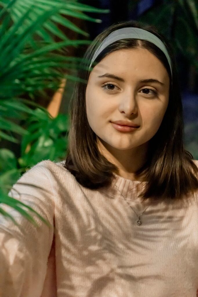 Young woman with headband taking selfie amidst lush greenery in Baku, Azerbaijan.