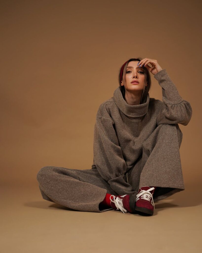 Fashionable woman in brown outfit sitting on floor, striking a relaxed pose.
