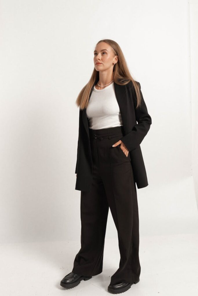 Fashionable woman in black suit and white top posing confidently in studio setting.