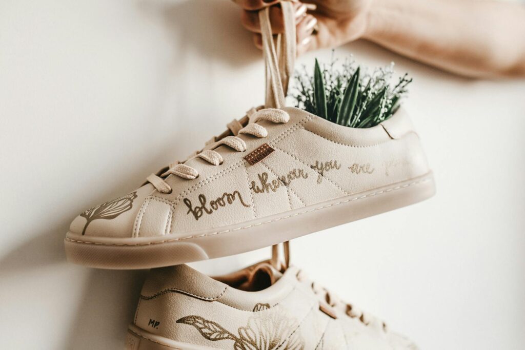 Close-up of beige sneakers with plant design and 'bloom where you are planted' script.