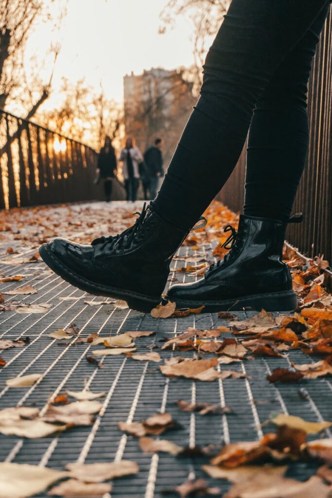 Stylish black boots on a metal grid walkway with fallen autumn leaves in the background.