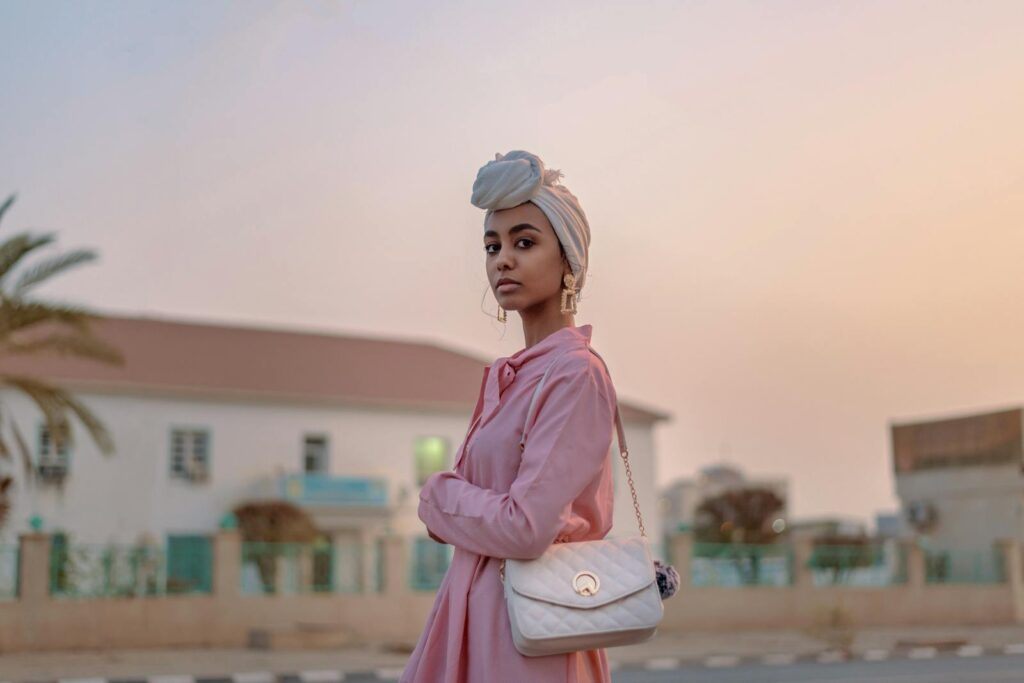 Stylish woman in pink dress with turban, posing outdoors at sunset.