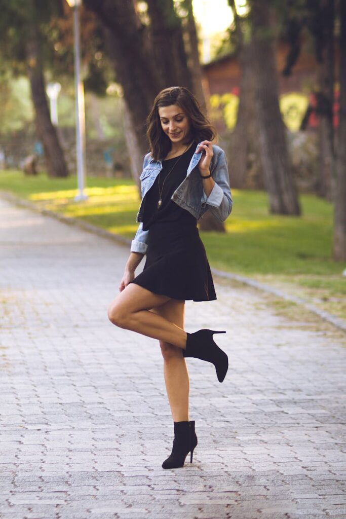 A stylish woman in ankle boots and denim jacket poses in a park in Thessaloniki, Greece.
