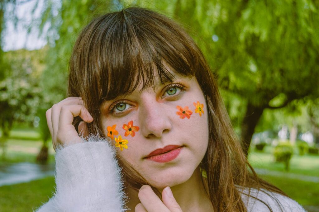 Young woman outdoors with floral face paint, showcasing beauty and style.