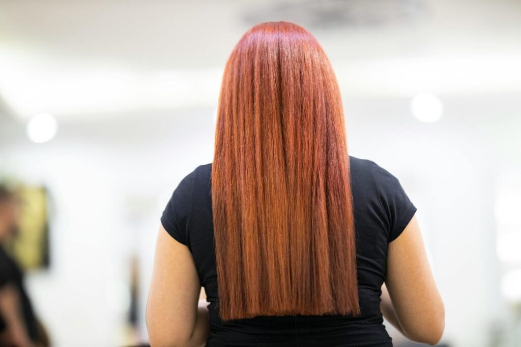 A woman with straight, vibrant red hair seen from the back, showcasing a fresh hairstyle in a professional salon.