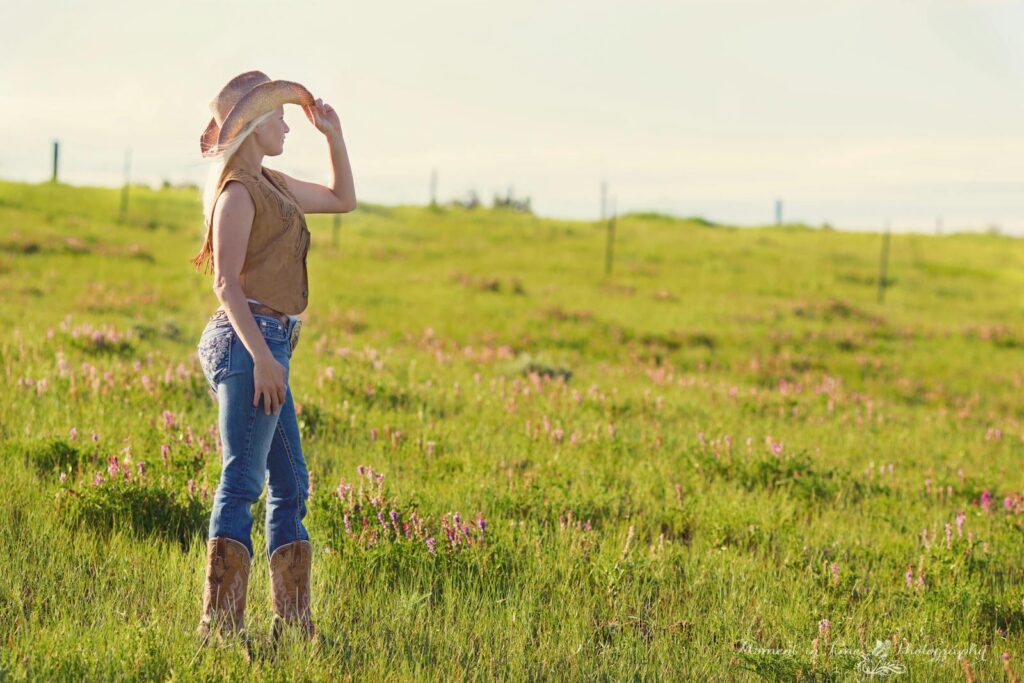 A woman wearing a cowboy hat stands in a sunlit countryside field.