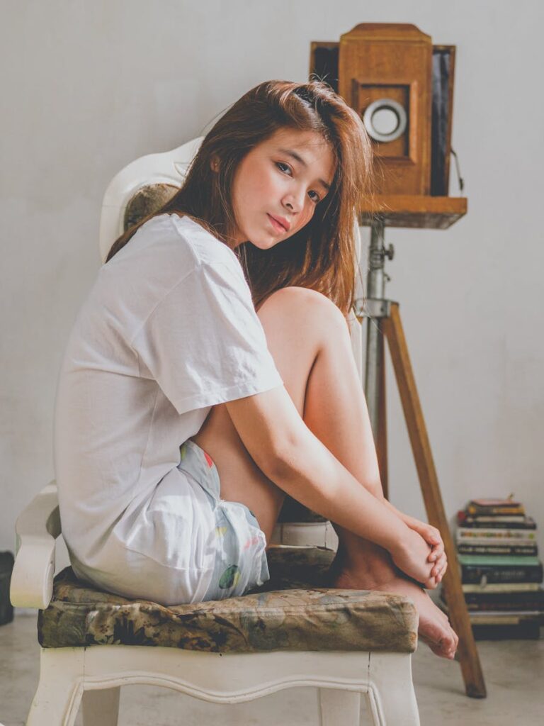 Stylish young woman relaxing on chair indoors, with vintage camera in background.