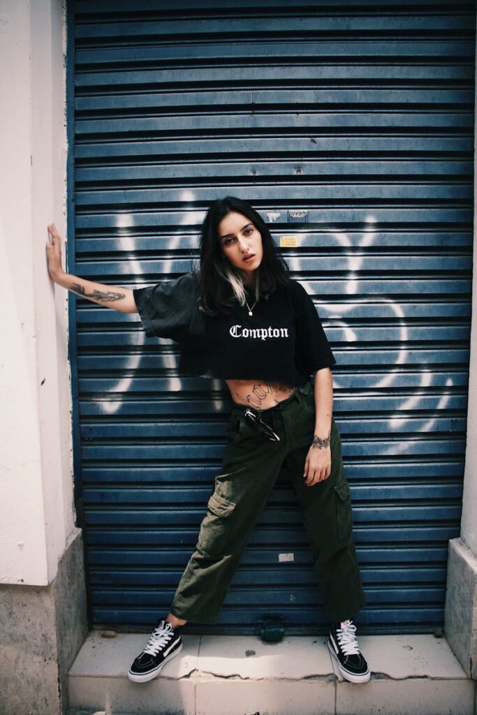 Urban fashion model posing outdoors in casual street wear with graffiti backdrop.