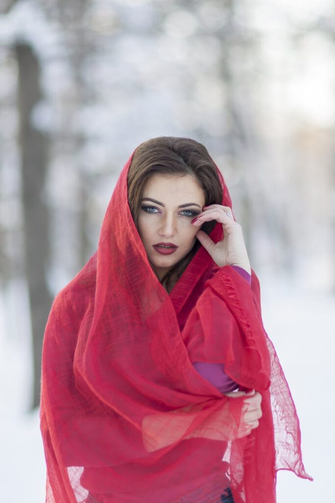 Outdoor portrait of an elegant woman in a red hijab posing against a winter background.