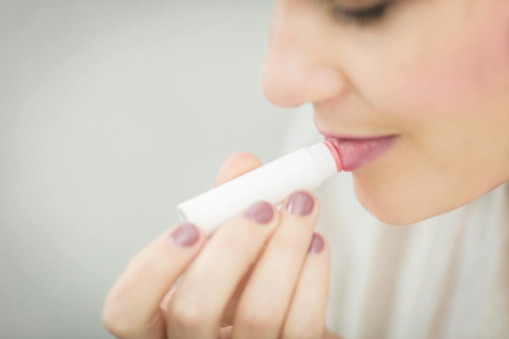 A woman applies lip balm for moisturizing her lips, focusing on health and beauty.