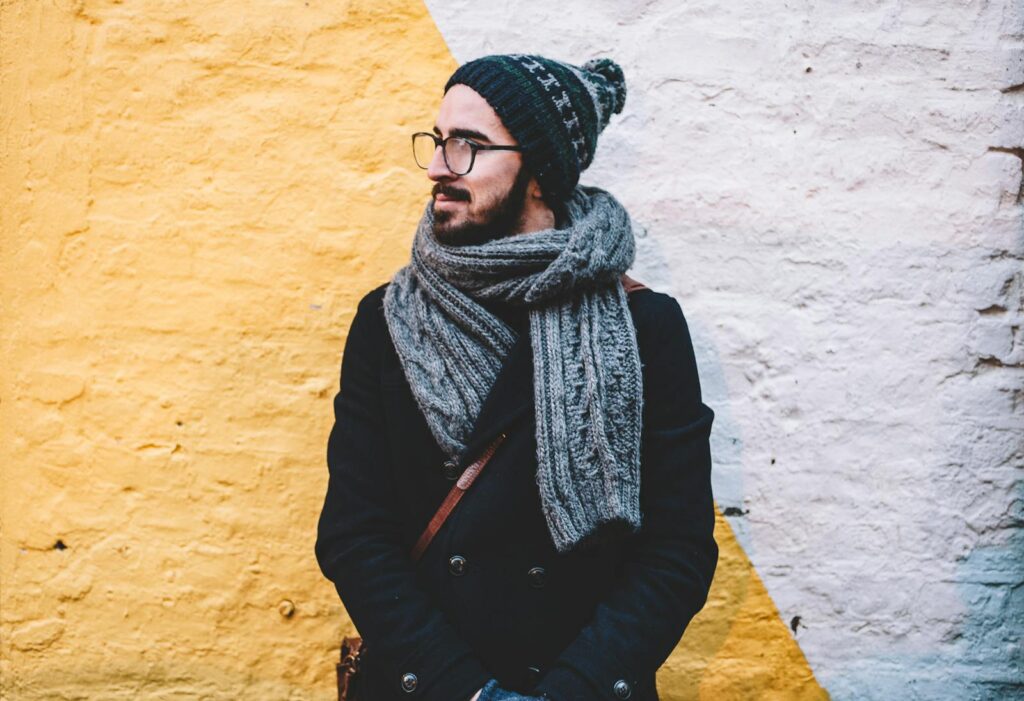 Man in winter attire with scarf and beanie looks away from camera against a vibrant wall.