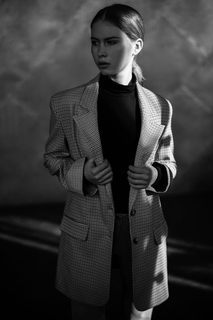 A stylish woman in a checkered blazer poses elegantly in a dramatic black and white portrait.