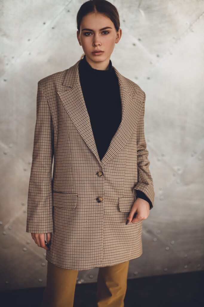 Fashionable woman in a blazer posing confidently against a neutral background. Indoor photo.
