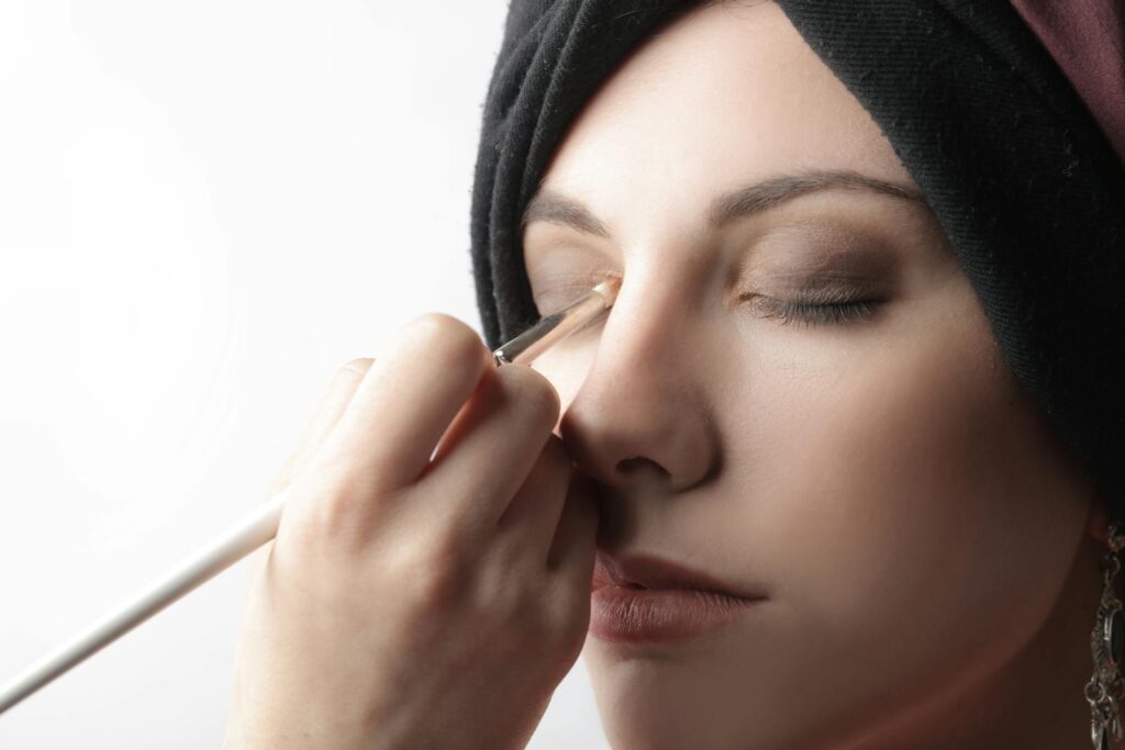 Elegant close-up of a woman applying eye makeup with a brush indoors.