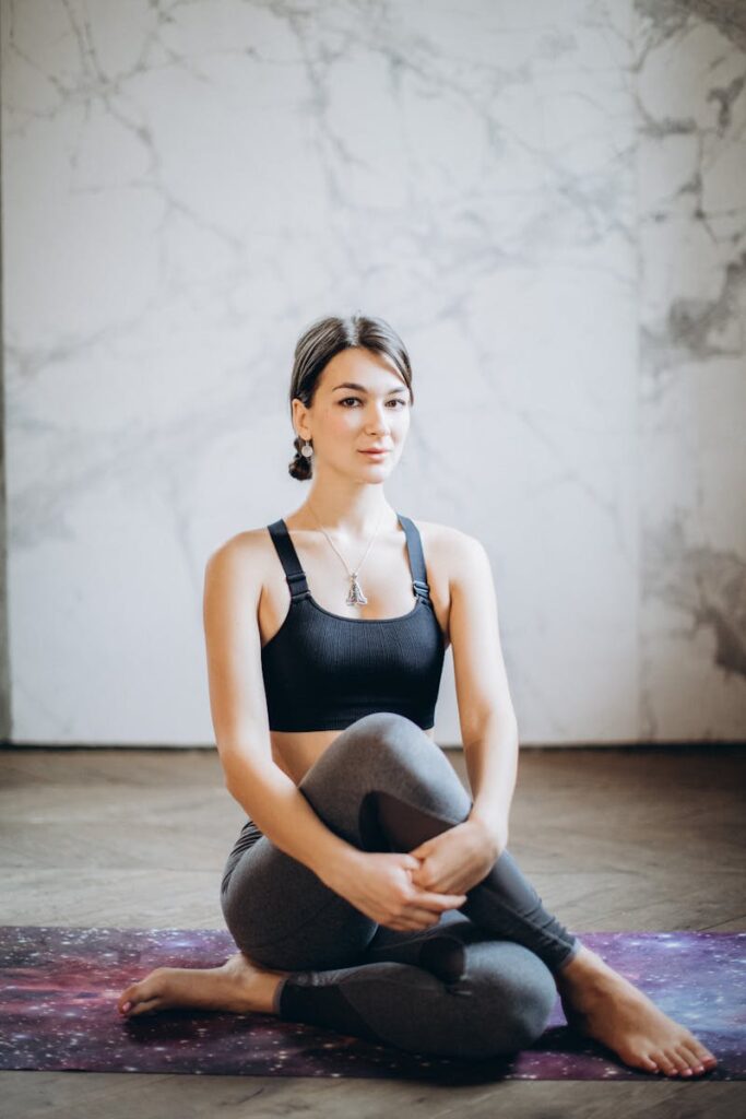A woman in activewear sitting in a yoga pose indoors, promoting fitness and mindfulness.