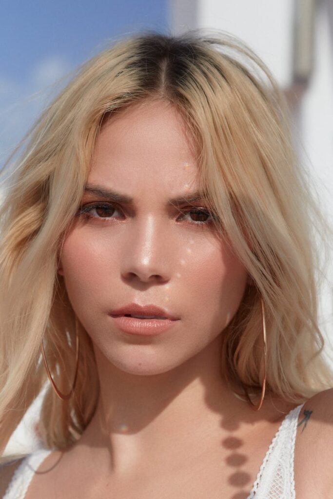 Close-up portrait of a young blonde woman with hoop earrings, serious expression, outdoors.