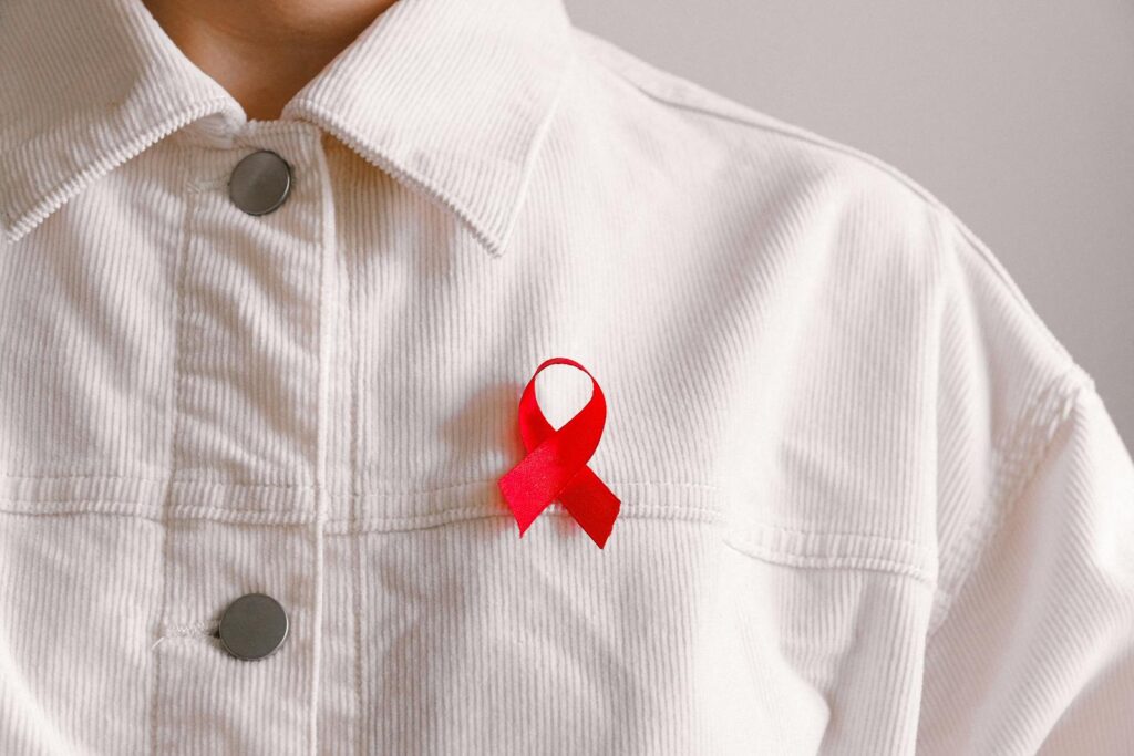 Red ribbon for HIV/AIDS awareness pinned on a white shirt symbolizing support and solidarity.