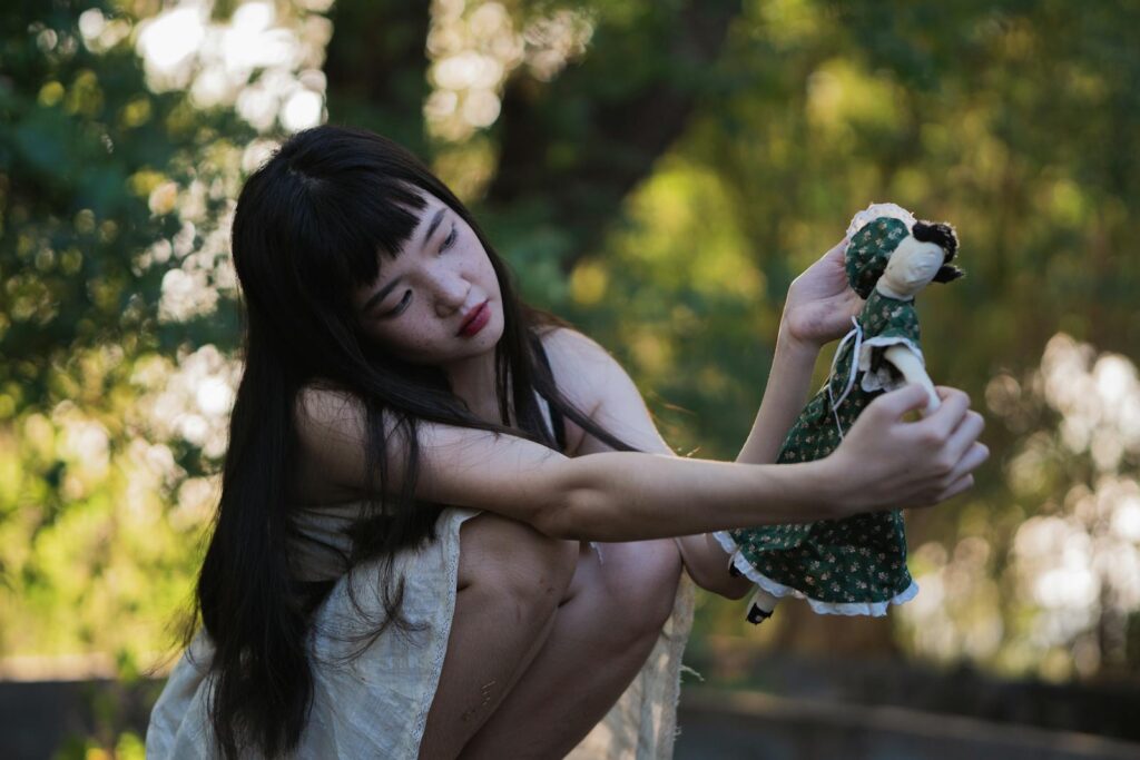 A young woman outdoors holding a doll, evoking themes of nostalgia and introspection.