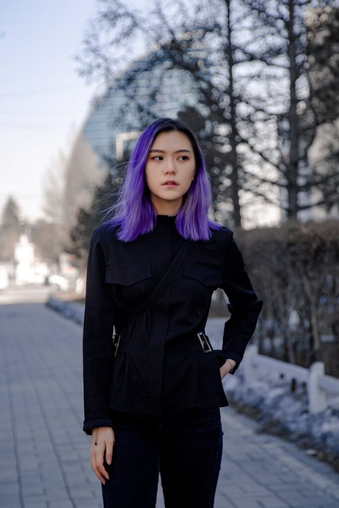 Portrait of an Asian woman with vibrant purple hair in a fashionable black outfit.