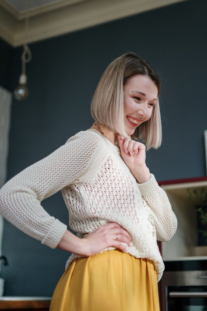 Charming woman with a bob cut smiling warmly in a cozy indoor setting wearing a knitted sweater.