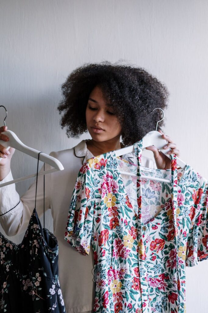 A woman with curly hair selects clothes, holding a floral dress indoors.